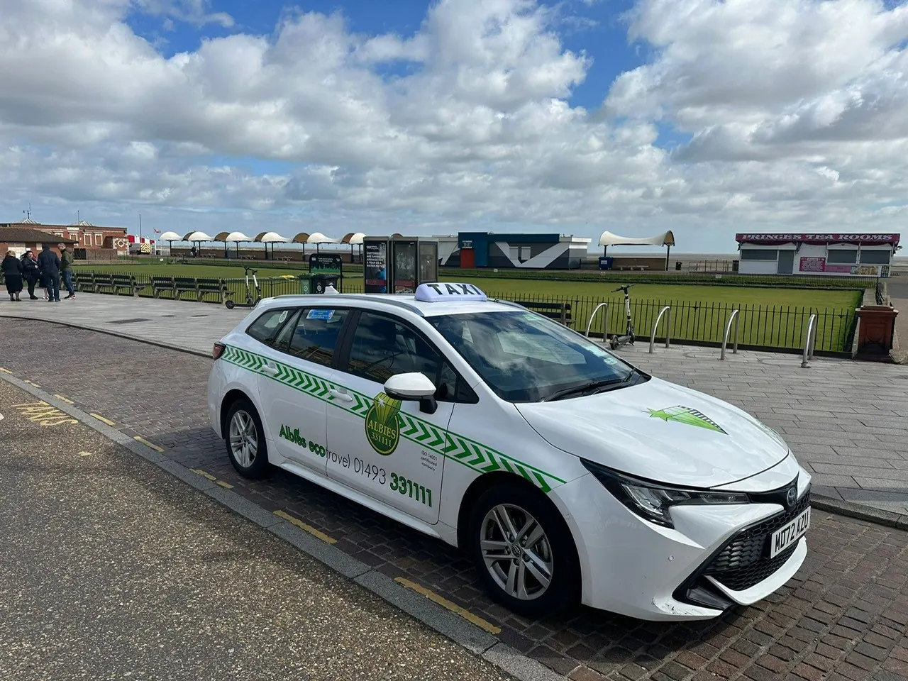 A white Albies eco travel hybrid taxi parked on Great Yarmouth seafront